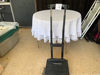 Expandable dolly with telescoping handle against a round table with a white lace tablecloth, showing front view.