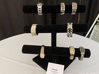 Black felt tri-tier watch stand holding 8 different wristwatches with metal bands.