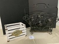 Photo showing black iron newspaper holder and white wooden flower box side by side on black background.