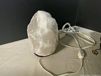 Close-up of white salt lamp with light glowing inside, wooden base, and attached power cord with switch.