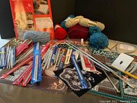 Wide view of lot showing crochet hooks, knitting needles, yarn skeins, and crochet pattern books.