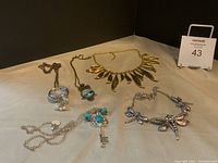 Photo showing 5 statement necklaces with various pendants and chain styles arranged on a light surface.
