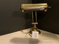 Vintage brass piano lamp with folding shade seen from front and side angles, showing decorative etched pattern and amber power switch.