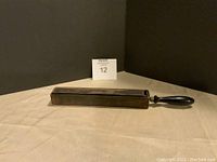 Full view of the vintage straight razor sharpener showing the rectangular stone and black handle on a beige surface.