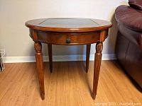 Front view of round wooden game table with carved legs and small drawer