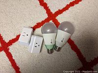 Photo of 2 TP Link smart LED lightbulbs and 2 smart plugs on carpet background with red pattern.