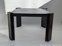 Front view of black wooden coffee table showing angled paneled legs and polygonal top surface with visible wood grain texture.