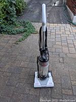 Front and full view of the Bissell PowerForce Lite upright vacuum cleaner, showing the handle, dust container, and base on a paved surface.
