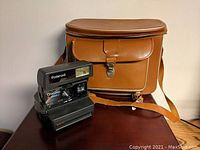 Polaroid OneStep CloseUp 600 instant camera alongside brown leather camera bag on a table.