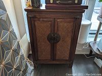 Front view of dark wooden cabinet with woven door panels and round metal latch, showing intact condition and wood grain.