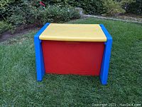 Fisher Price plastic toy box front view showing yellow lid, blue sides, and red base on grass.