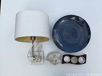 Overhead view of all items: plug-in wall sconce with white shade, dark blue round plate, curved wooden tealight holder with three glass holders, and a natural seashell
