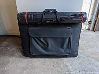 Front view of the black fabric portfolio bag with the extendable tube resting on top.