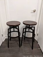 Pair of adjustable height industrial style bar stools with dark wood round seats and black metal bases, standing side by side.