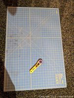Top view of blue Olfa 24x36 inch self-healing cutting mat with grid and rotary cutter placed on it.