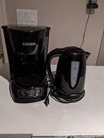 Black+Decker coffee maker and black electric kettle on a countertop with power cords visible.