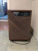 Front view of Mastercraft D28 dehumidifier showing diagonal vent pattern and control knob on front panel, brown finish.