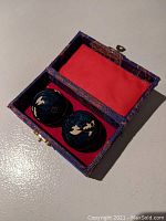 Open decorative fabric case showing two black Baoding balls with gold designs inside a red fabric lining