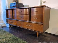 Side angled view showing the full wooden credenza with multiple drawers and brass hardware, highlighting curved drawer fronts and tapered legs.