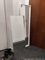Two full-length rectangular mirrors positioned leaning against a wall and door. One has a white frame, the other is frameless.