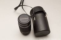Top view of the Pentax lens with case showing lens cap marked Pentax and cylindrical black leatherette case with strap.