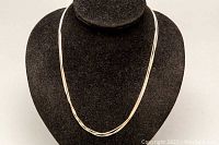 Full view of the triple strand silver necklace displayed on black jewelry stand showing the overall length and design.