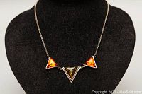 Front view of the necklace displayed on a black bust showing the three amber triangular pendants with silver setting and chain.