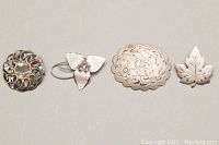 Four silver brooches arranged side by side on a gray background to show overall lot.