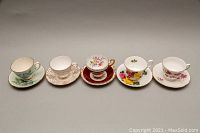 Five Royal Albert teacup and saucer pairs showing top view of cups and saucers with floral patterns and gold trim.