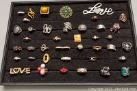 Full tray view showing assortment of 42 costume rings with varied designs, some with missing stones, wear evident.