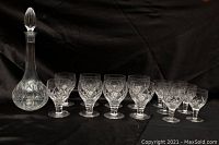 Set of 8 larger and 6 smaller Stuart England cut crystal glasses arranged with the tall lidded decanter on a black background