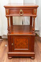 Frontal view highlighting the drawer with brass ring pulls and the cupboard door with keyhole and decorative wood inlay.