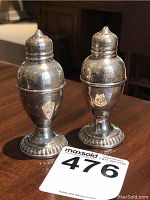 Pair of vintage sterling silver salt and pepper shakers on wooden table with auction lot card.