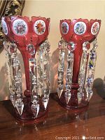 Overall view of both ruby glass candle holders with dangling crystal prisms on wooden surface