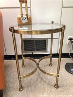 Side view showing round brass frame with a clear glass top and four legs connected by a curved X shaped brace near the bottom.