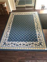 Full view of rectangular area carpet showing blue diamond lattice pattern on the central field and the cream border with blue floral vines.