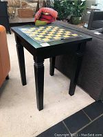 Full view of the black wooden games table with checkerboard top, standing on four straight legs.