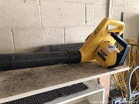 Full side view of the yellow leaf blower vacuum on a wooden shelf against a cinderblock wall.