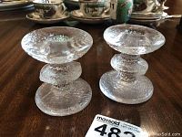 Pair of small clear textured glass candle holders with rounded base and top, visible textured detail and overall design from front angle on wooden table.