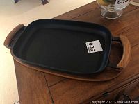 Top angle view of black cast iron griddle on teak base showing handles and smooth cooking surface.