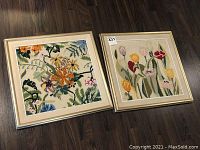 Photo of two needlepoint floral still life artworks side by side on floor, both framed 18x18 inches