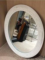 Full front view of oval mirror showing white decorative frame and reflective surface.