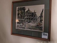 Framed Parisian art print showing a street and architectural scene.