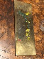 Full top view of the rectangular brass scroll weight showing engraved oriental characters and floral painting on right side.