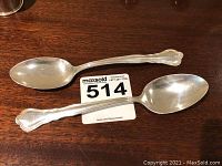 Two full-length sterling silver spoons placed on a wooden surface showing overall size and design.