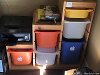 Photo showing wooden storage shelf with plastic bins in multiple colors and items on top including printer and office supplies