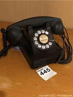 Front and side view of vintage black Bakelite rotary dial telephone on wooden surface.