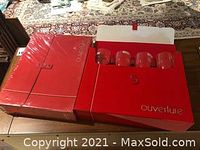 Two unopened red boxes with four crystal wine glasses each, one box partially open showing glasses inside.
