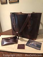 Dark brown leather tote bag with straps and matching leather change purse, card, and storage bag on a wooden table.