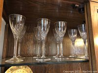 Eight crystal wine goblets sitting on a shelf with visible cut-glass facets and long stems.